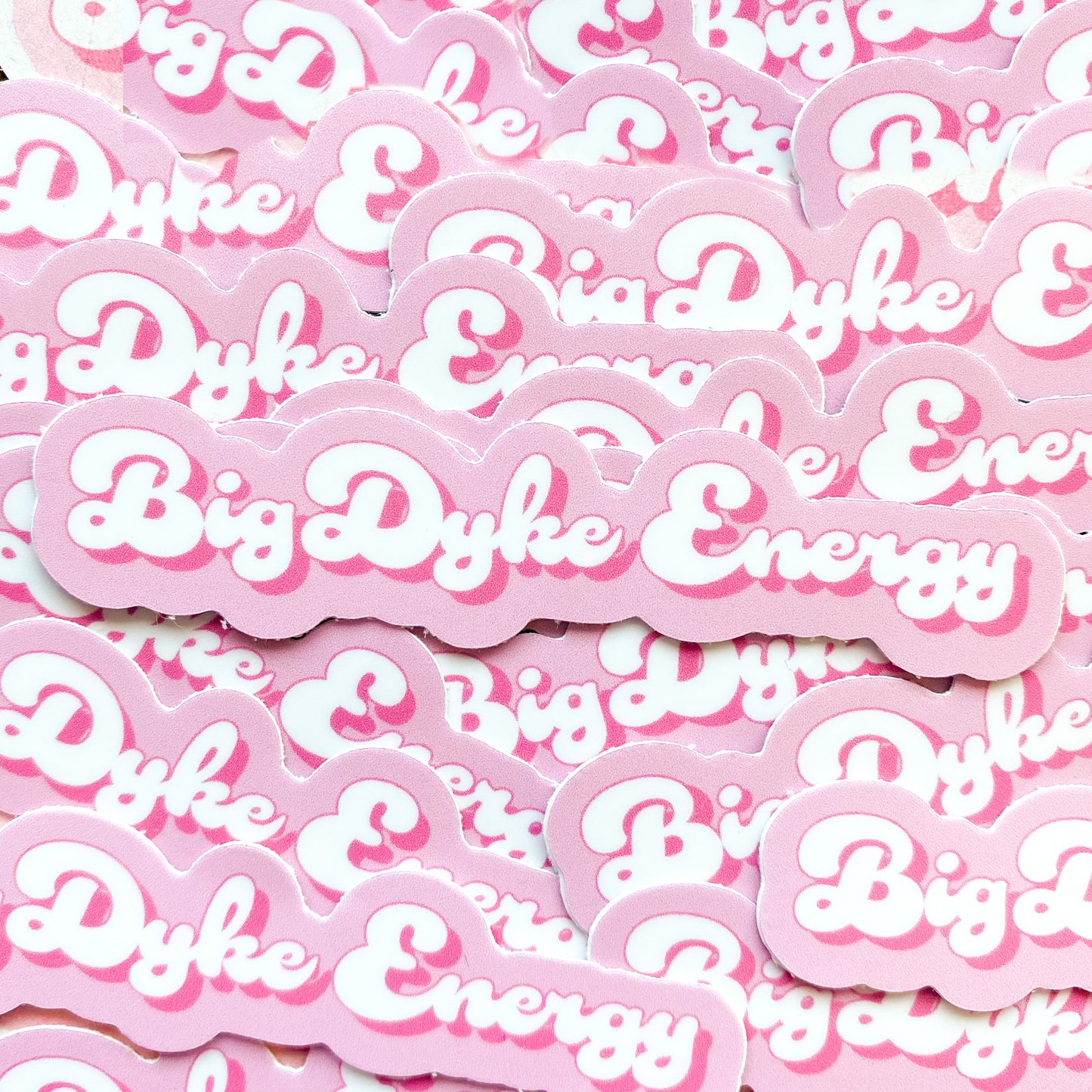 Photo of pink and white sticker with the  words 'big dyke energy', a funny lesbian pun.